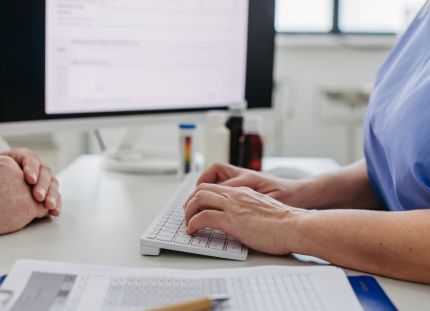 Hoitaja keskustelee potilaan kanssa. Taustalla tietokoneen näyttö.