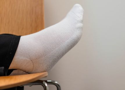 Jalka lepäämässä tuolin päällä. Näkyy vain hiukan lahjetta ja valkoinen sukka.