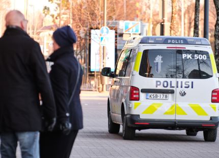 Poliisiauto katukiveyksellä. Vieressä muutama ihmishahmo selin kameraan päin.