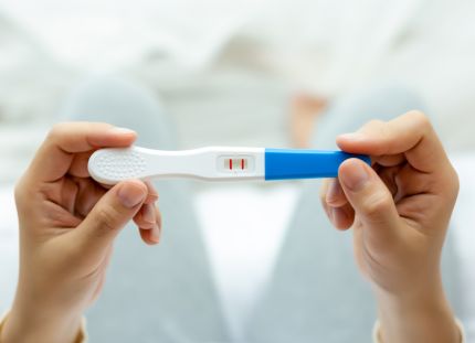 Henkilö pitää kädessään positiivista raskaustestiä.