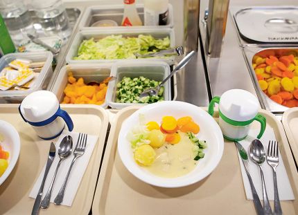 Päiväkodin ruokalinjastolla tarjottimilla annoksia valmiina. Lautasella perunoita ja vihanneksia.
