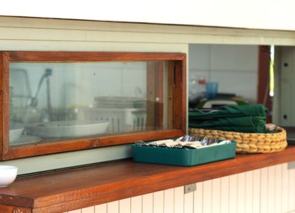 Kuva ruokalinjaston luukku ja pieni ikkuna, josta näkee läpi keittiöön.