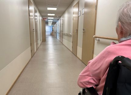 Palvelutalon pitkä käytävä ja vanhus pyörätuolissa.