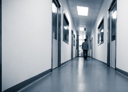 Pitkä, tyhjä käytävä, jonka päässä yksi henkilö kävelee poispäin valaistua ikkunaa kohti.