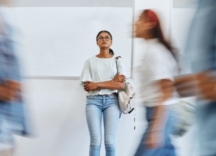 Nainen seisoo kiirehtävien ihmisten keskellä stressaantuneena kädet puuskassa ja katsoo ylöspäin.