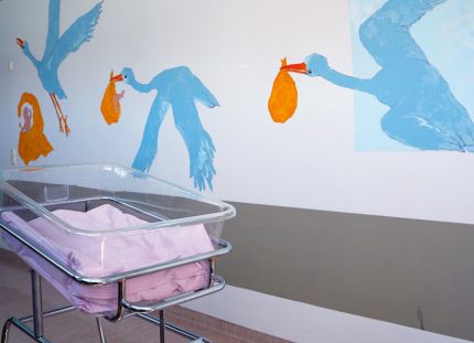 Vauvan sänky sairaalan käytävällä. Seinällä piirroskuva haikarasta.