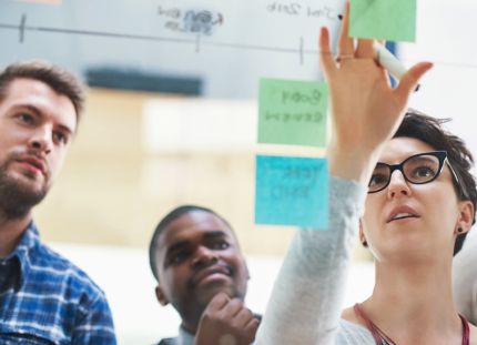 Työtiimi tekee suunnittelutyötä yhdessä kiinnittäen post it -lappuja lasiseinälle.