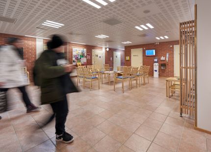 Terveyskeskuksen odotustila. Muutama ihminen epätarkkana kuvan etualalla kulkemassa huoneen läpi.