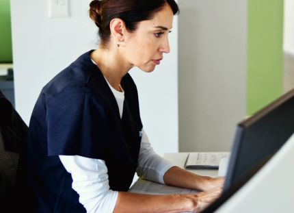 Hoitaja klinikan tietokoneella katsoo vakavana näyttöä.