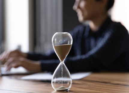 Ihminen läppärillä, etualalla tiimalasi.