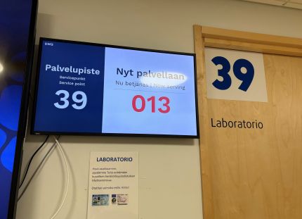 Työterveyshuolto maksoi noin 600 euroa työntekijää kohti. Yksityisen lääkäriaseman odotustila ja vuoronumerot television näytöllä.
