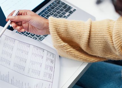 Nainen tarkastelee paperisia tositteita. Ansiopäivärahan porrastus näkyy, kun työttömyys pitkittyy.