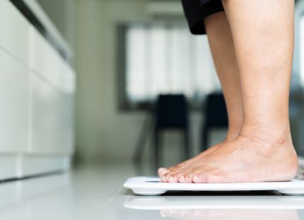 Henkilö seisoo keittiössä vaa'an päällä punniten itsensä. Tutkimus: Painon kehityksen seuranta voi auttaa tunnistamaan tyypin 2 diabeteksen riskipotilaita.