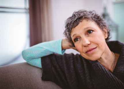 Hieman hiuksista harmaantunut nainen nojaa käteensä ja katsoo ikkunasta ulos.