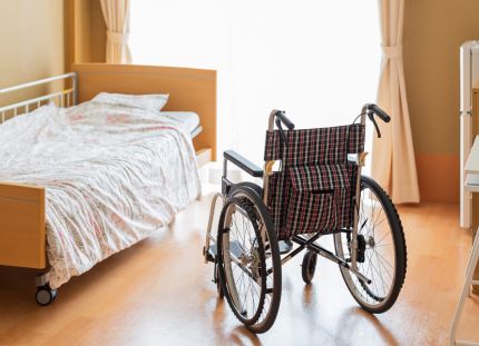 Asukkaan huone vanhainkodissa. Sänky ja pyörätuoli ikkunan ääressä.