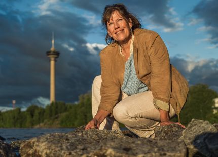 Ulla Ollikkala kyykyssä rantakivikossa, taustalla Tampereen Näsinneula.