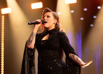 Tampereella työskentelevä sairaanhoitaja Justiina Luukaslammi on edennyt The Voice of Finlandissa semifinaalivaiheeseen. Justiina laulaa mikrofoniin tummassa dramaattisessa mekossa.