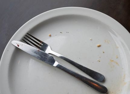 Tyhjä lautanen, jossa näkyy vielä ruoan murusia. Haarukka ja veitsi aseteltuna lautasen päälle.