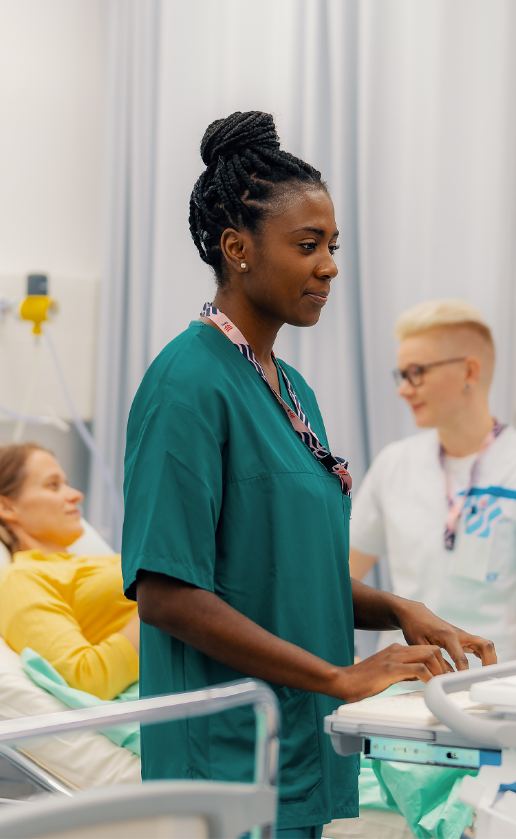 Hoitaja käyttämässä monitoria ja taustalla potilas ja toinen hoitaja