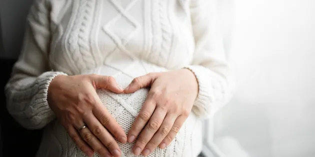 naisen raskausvatsa ja kädet sen päällä sydämen muodossa