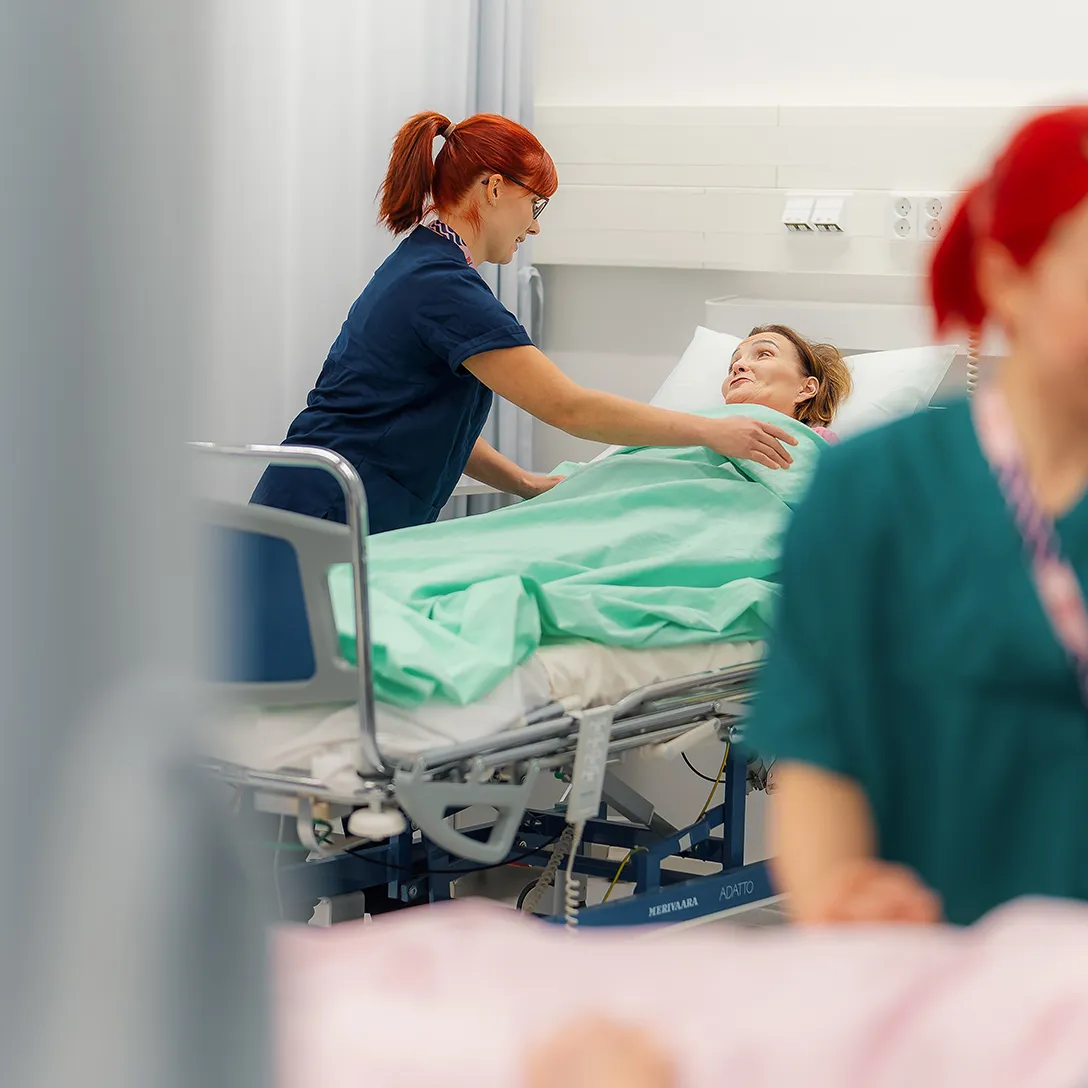 Kuvassa hoitaja peittelemässä asiakasta potilasvuoteessa