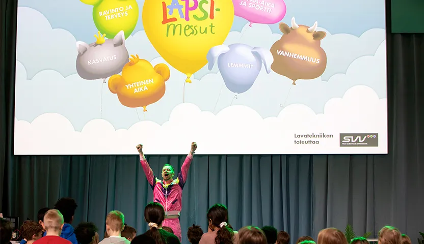 Lapsimessujen esiintymislavalla juontaja ja yleisöä